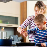 Nainen ja poika tekevät yhdessä ruokaa, paistavat pannulla jotain.